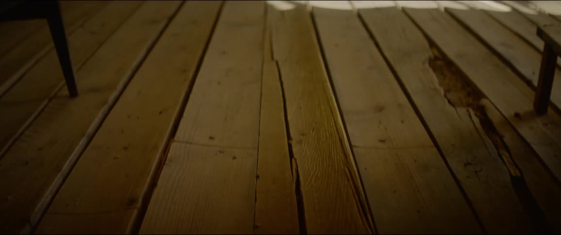 Chairs and a table sit on uneven wooden planks in front of a window