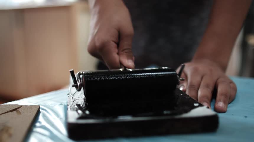 Man uses a roller to spread black ink on a tablet