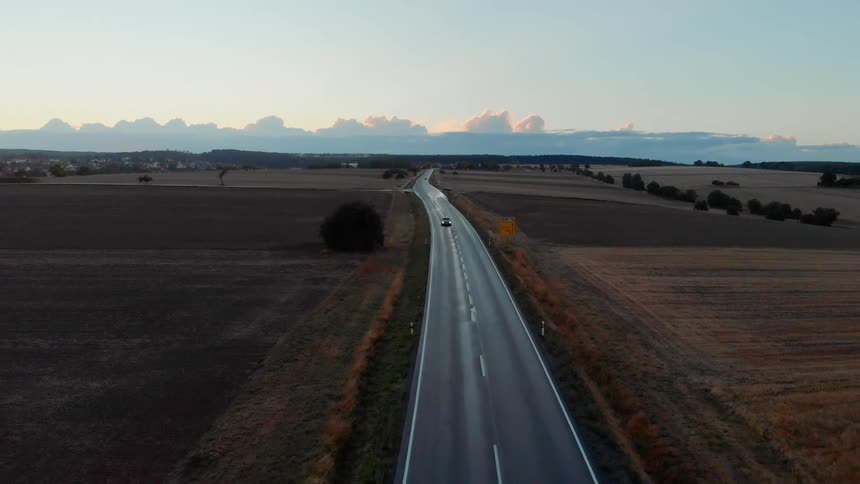 A car drives down a two lane highway through a rural area