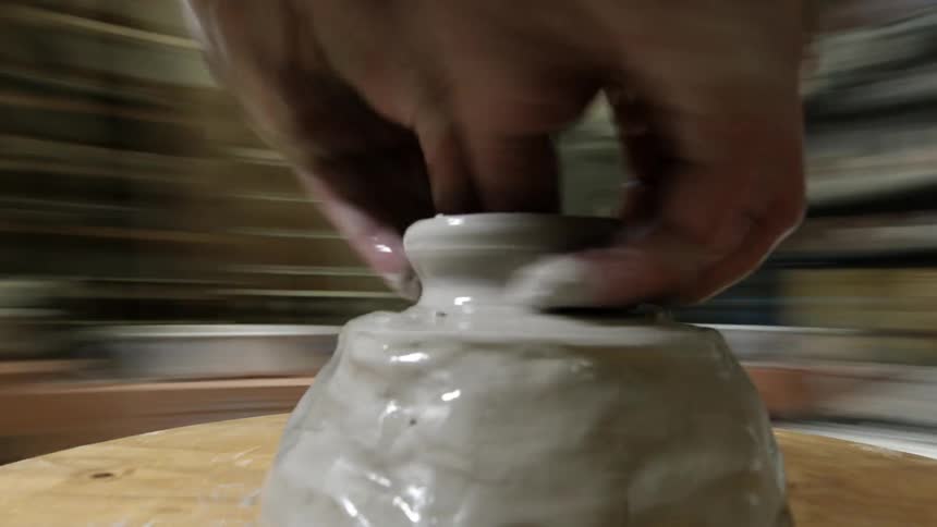 A hand shaping a clay pot on a pottery wheel
