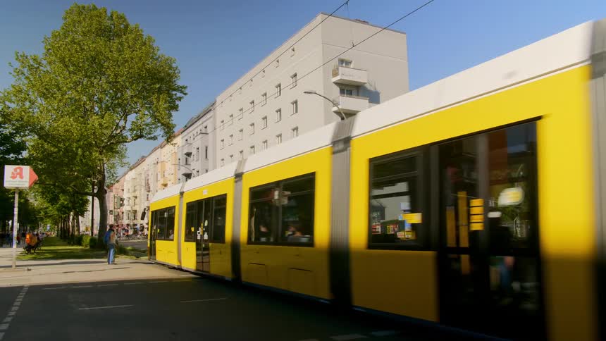 Yellow tram carrying passengers moves along metal lines in the road in a city