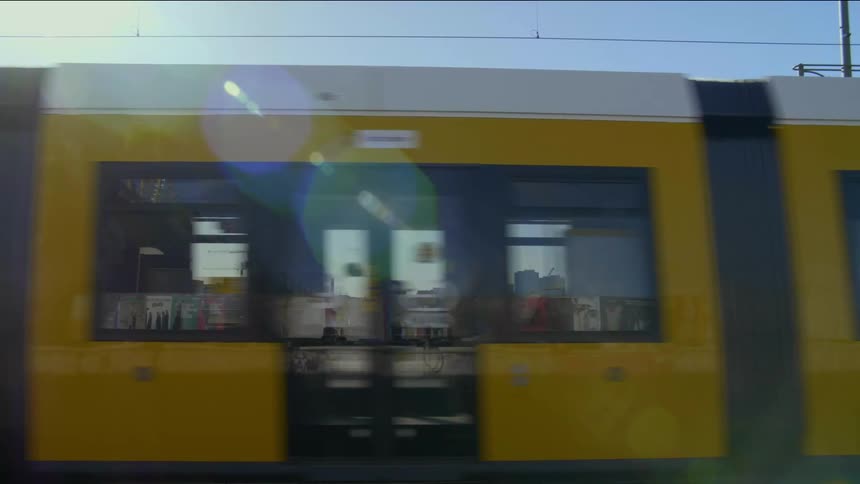 Yellow tram carrying passengers moves along metal lines in the road in a city