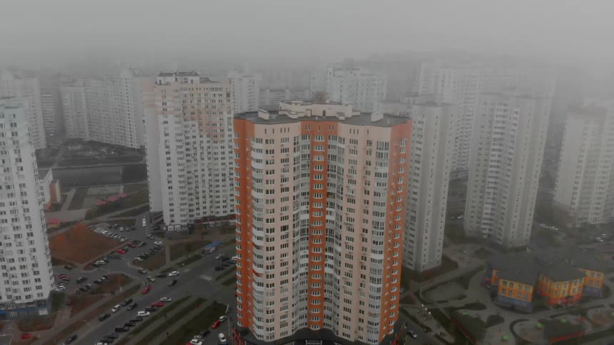 Fog hangs over tall similar looking city buildings as cars travel on streets below