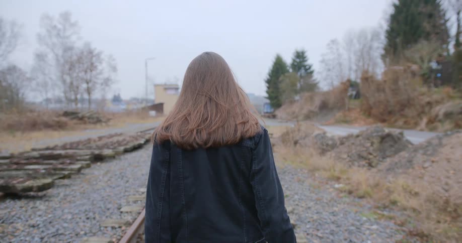 A young woman walks on train tracks in a rural area
