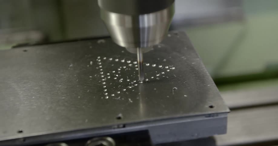 A machine drills holes through a piece of metal that form a triangle design