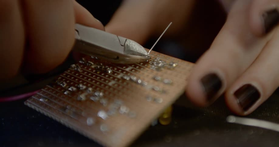 Woman uses pliers to cut a wire on an electronic board