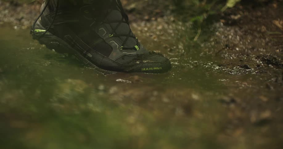 Black hiking boot stepping in a mud puddle on a dirt trail