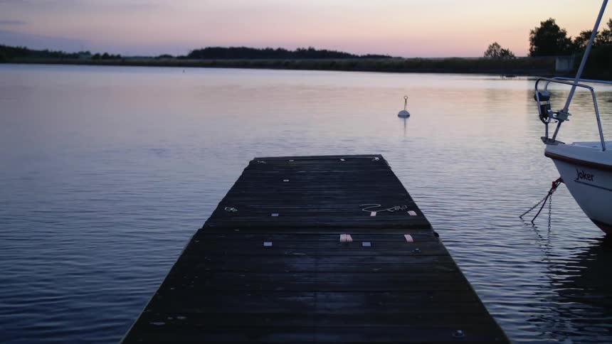Buoy floating on the quiet surface of a lake near a pier and boat at sunset