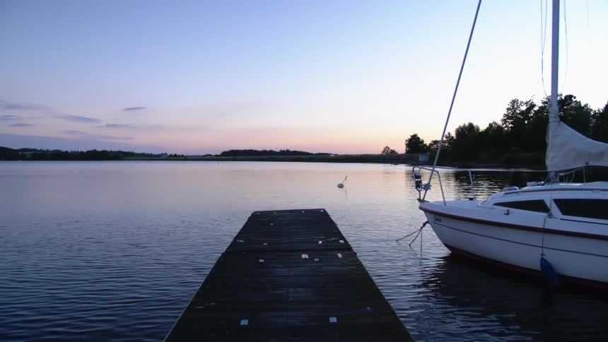 A sailboat is anchored in a lake next to a wooden dock at sunset