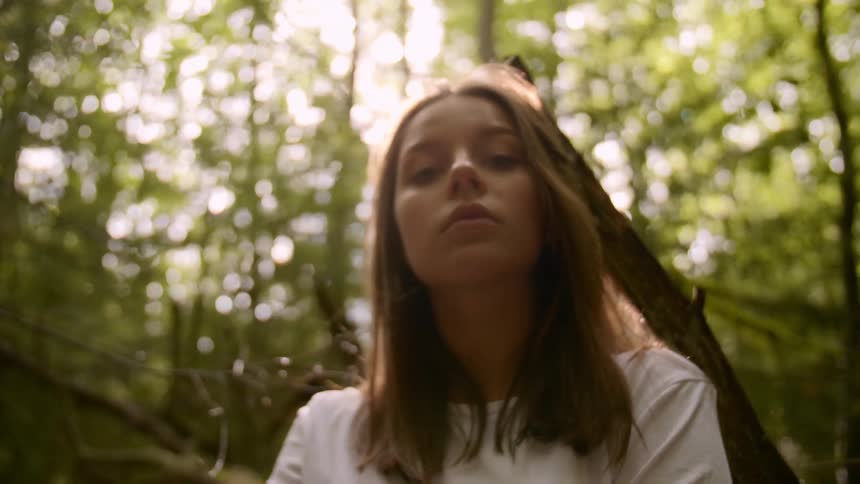 Young woman in a forest looks at the camera while sunlight filters through tree branches