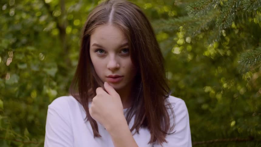 A young woman stands in front of trees and runs her hand through her hair