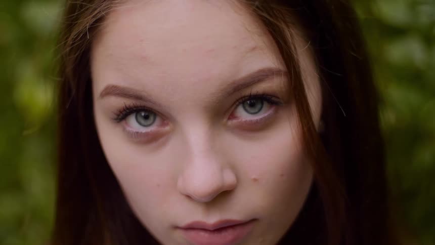 Woman with long brown hair blinks her eyes as she looks straight ahead