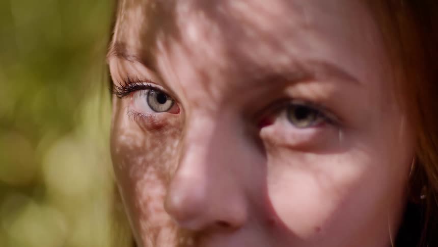 Young woman brushes hair back out of eyes and looks up toward the sun