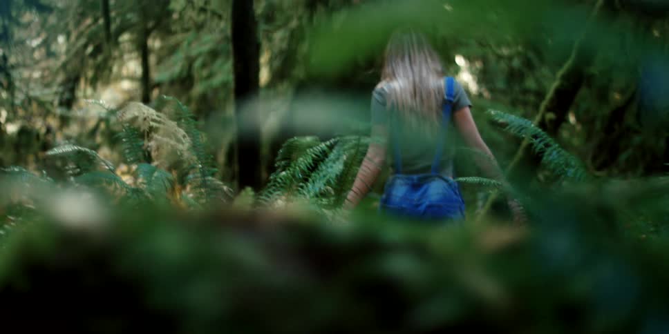 Blonde woman with shoulder strap jeans walks in the woods