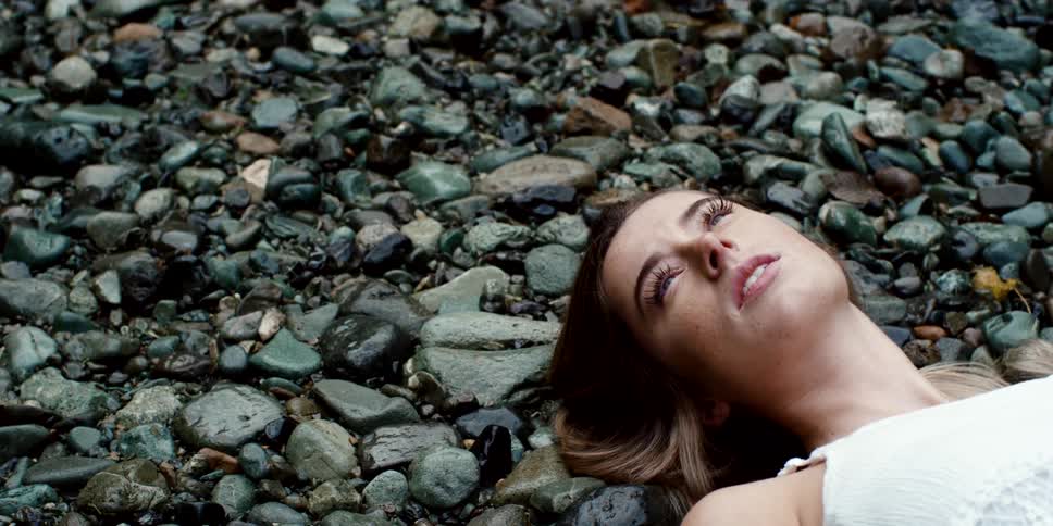 A woman in a white dress lies on a rocky surface