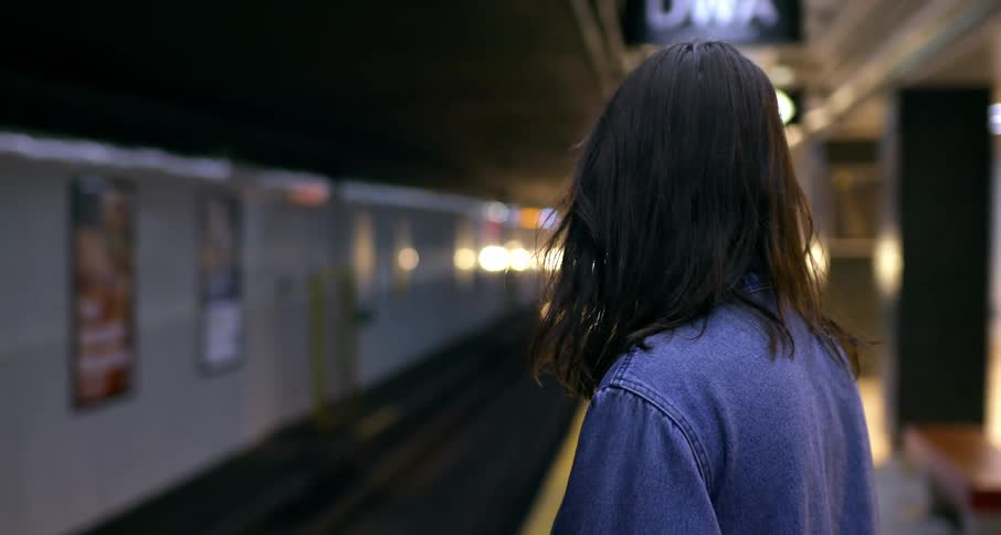 A young woman waiting on the subway platform, her hair blows in the wind from the approaching train