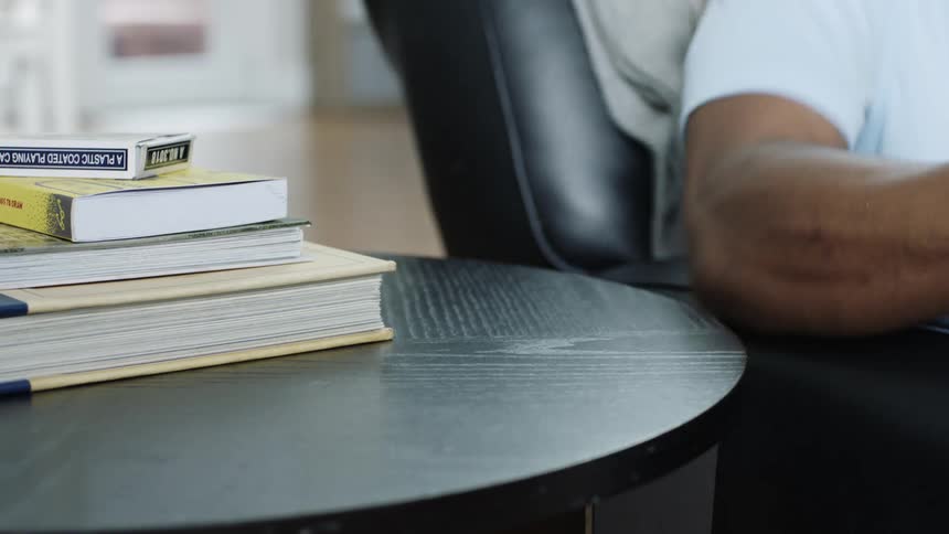 Black man with a white shirt sits in an black armchair picks up a smartphone from a black occasional table