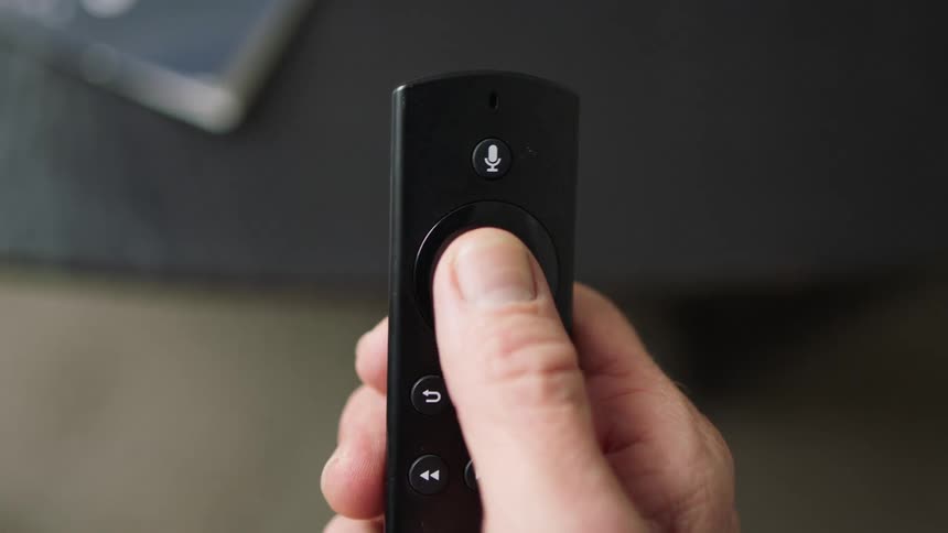 A mans hand uses a black tv remote control