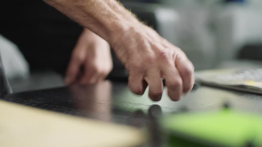 A man lifts a television remote from a table as he takes a seat on a sofa