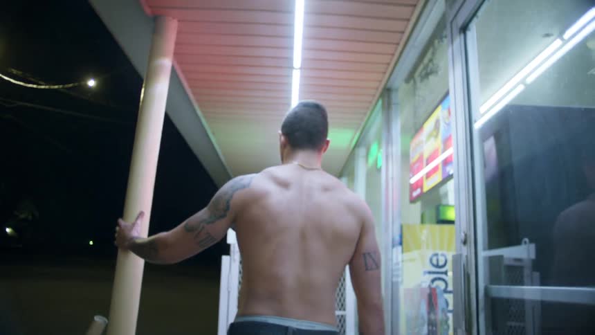 A shirtless man paces in front of a convenience store