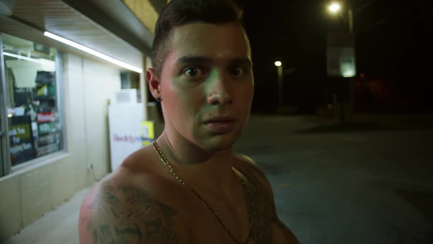 A teenager stands on a street without a shirt