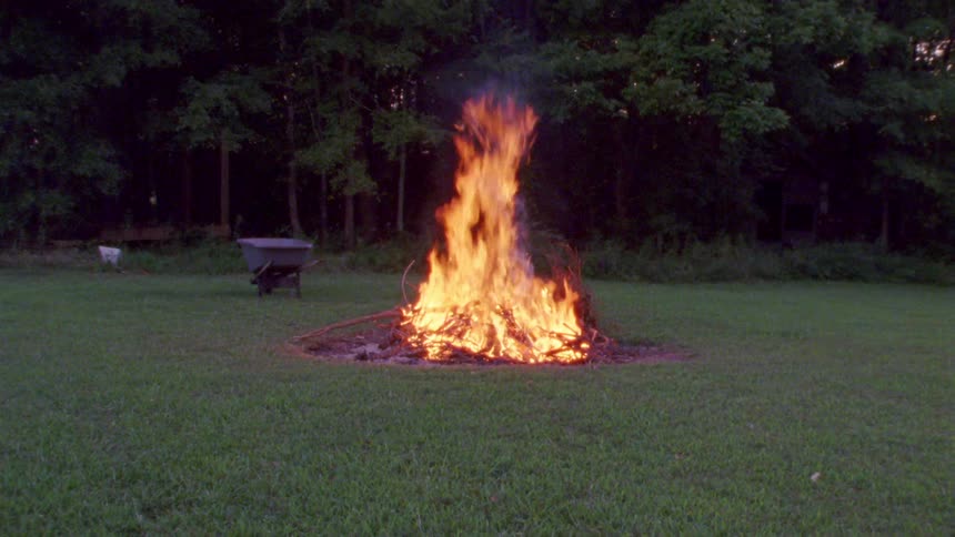 Bonfire burning in middle of lawn in a woodsy area