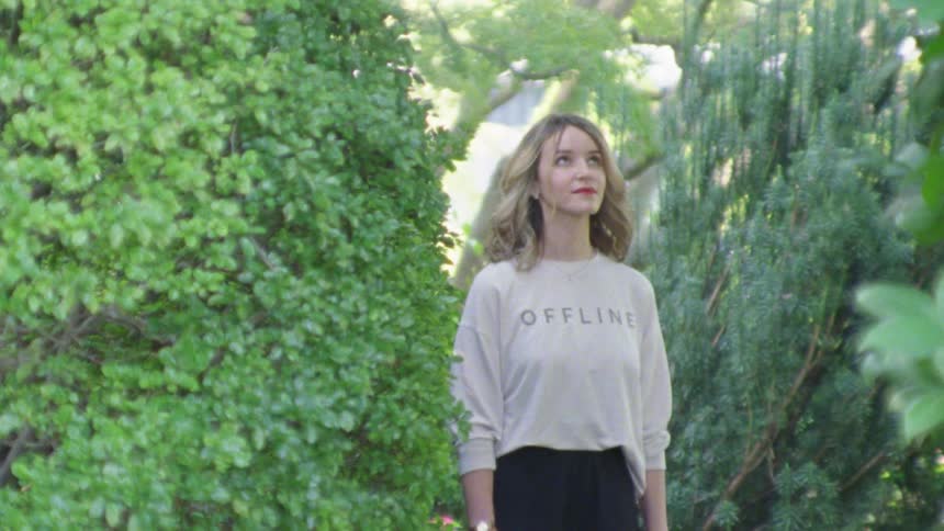 A woman smiles as she looks up at the tall trees surrounding her
