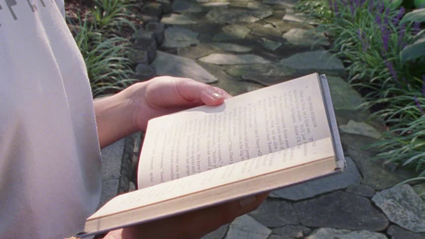 Woman reads a book while standing on a stone path
