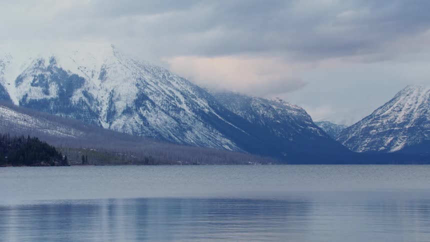 Snow covered mountain peaks under the clouds near the calm waters of a lake