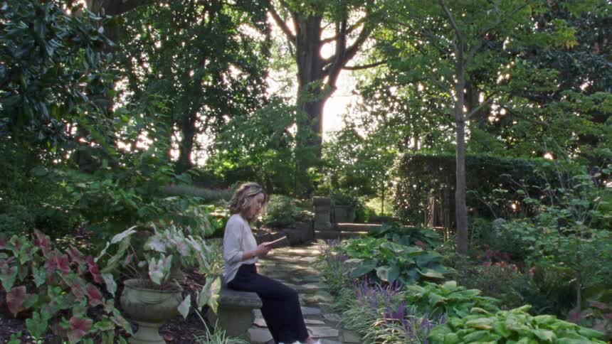 A woman sits on a bench reading a book in a public park garden