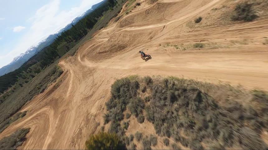 Dirt bike rider rides the bike on a dirt trail then jumps it over a hill