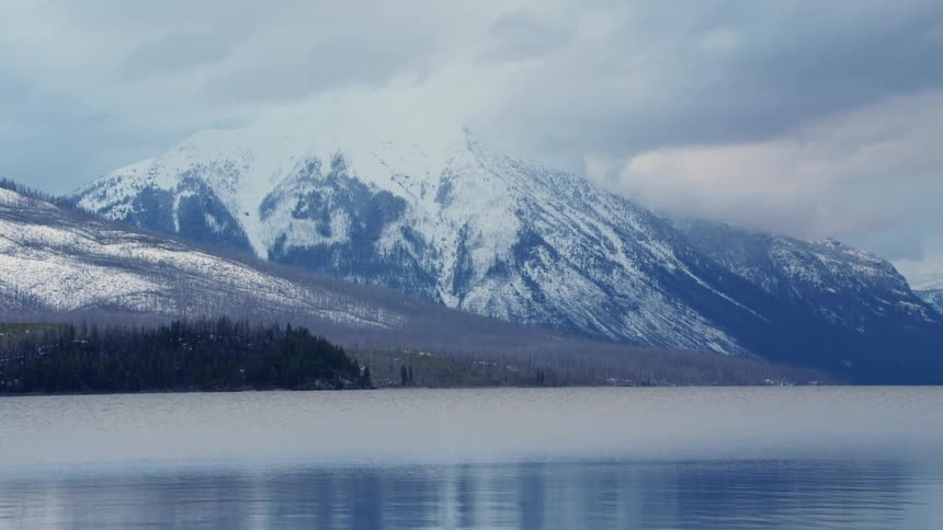 A lake at the base of a snowy mountain range on a cloudy day
