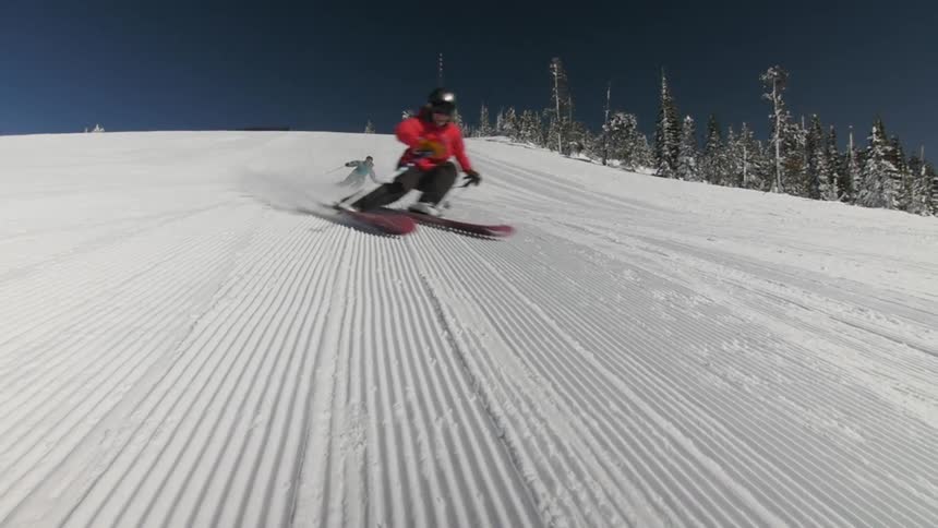 Two people ski down a snow covered mountain