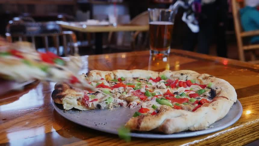 A persons hand taking a piece of pizza on a table in a restaurant