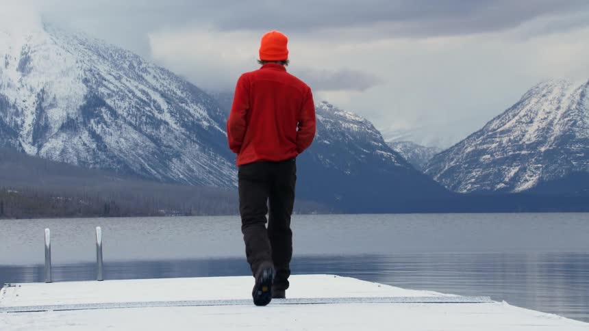 Man wearing a toque walks on a dock over the lake near the snowy mountains