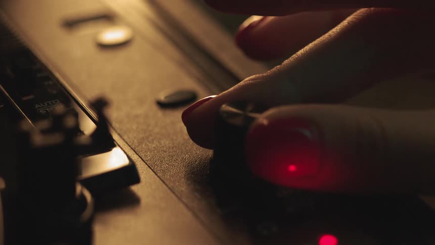 Person turns a dial on a turntable in a dimly lit room