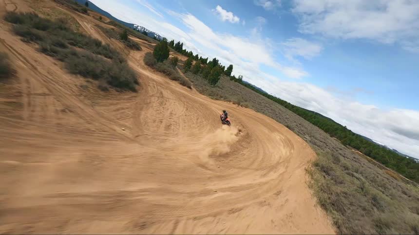 A person rides a dirt bike on a dirt track in a rural terrain