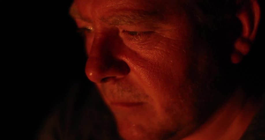 Middle aged man watches a campfire at night
