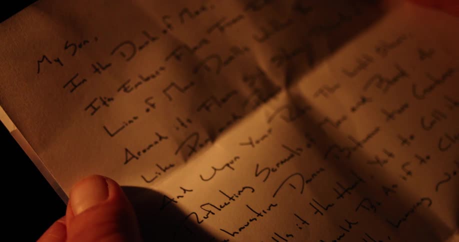 Man sitting by a campfire reads a letter