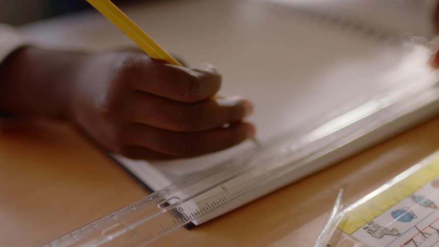 A black child uses a ruler to draw a straight line in a notebook