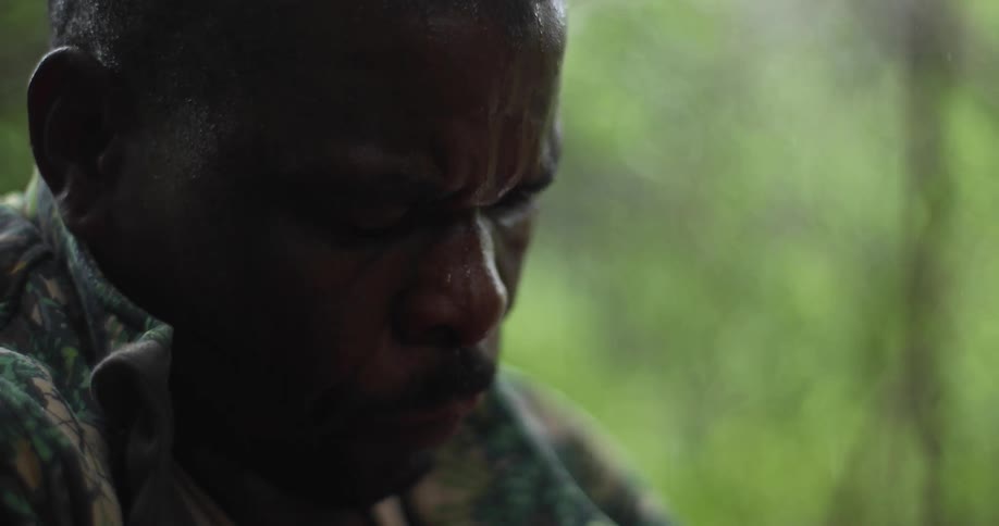A man is chopping something with a machete while it rains