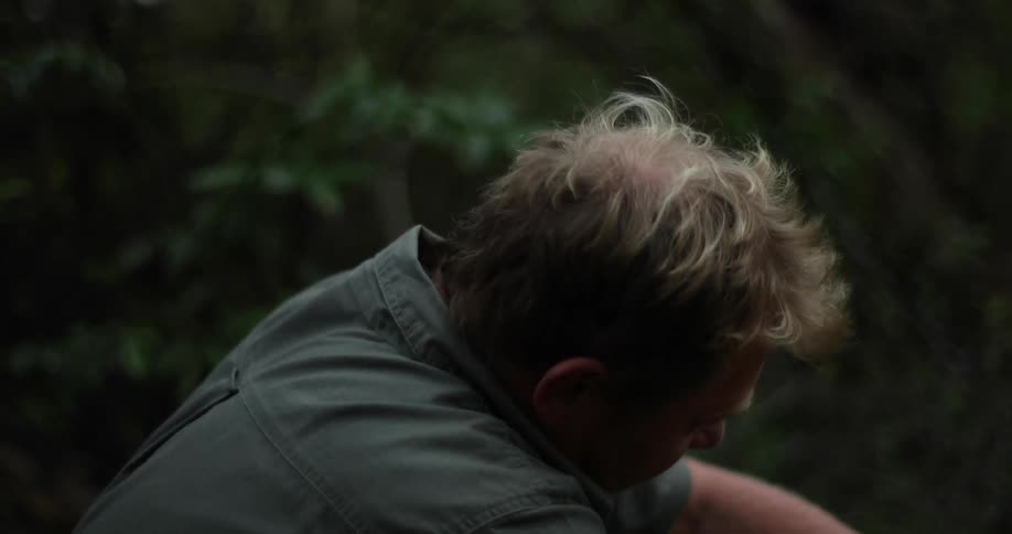 Man sitting on a forest manipulates objects outside the frame