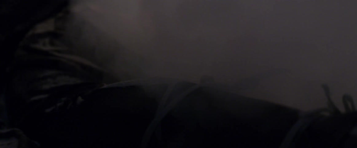 Smoke surrounds a body tied in a black tarp as flames grow brighter