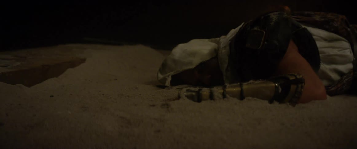 Man wearing robe and armour lays on the sand surrounded by flashing lights