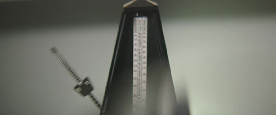 A person flicks the pendulum of a metronome causing it to begin swinging back and forth