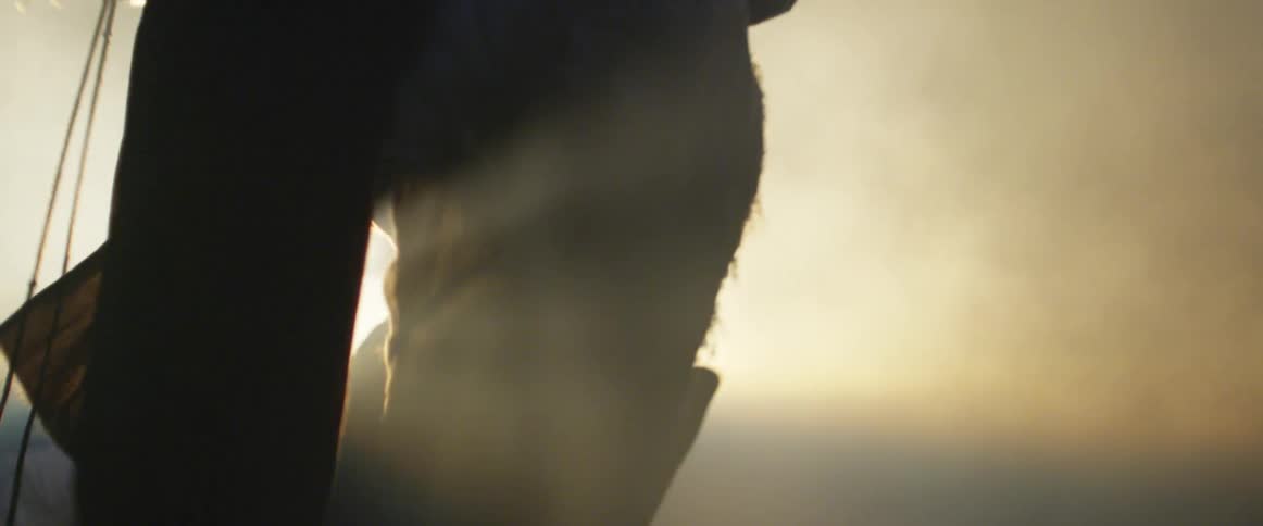 A man wearing a cloak and a large belt strides through smoke