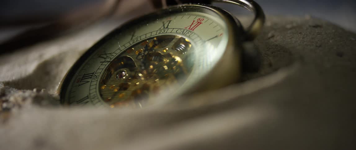 Pocket watch nested in the sand on the floor in a dimly lit room