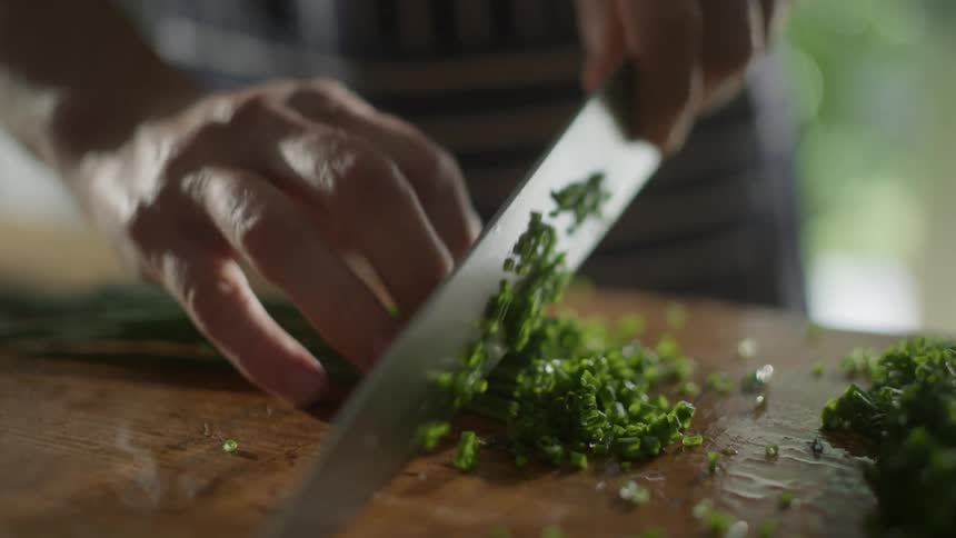A person chops herbs with a large knife
