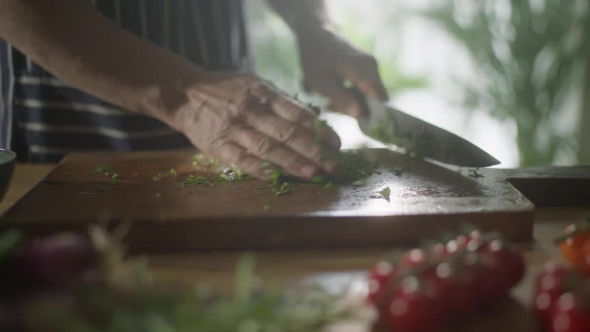 A person uses a knife to chop fresh herbs on a cutting board