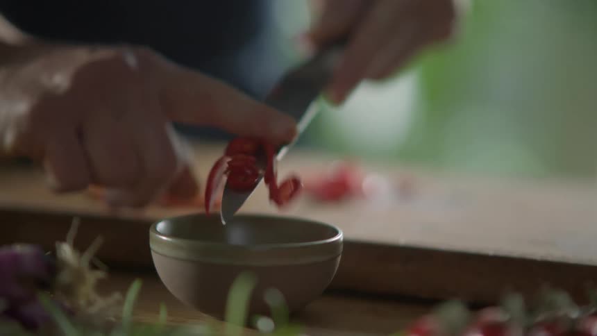 A man wipes vegetables off a knife as he cooks
